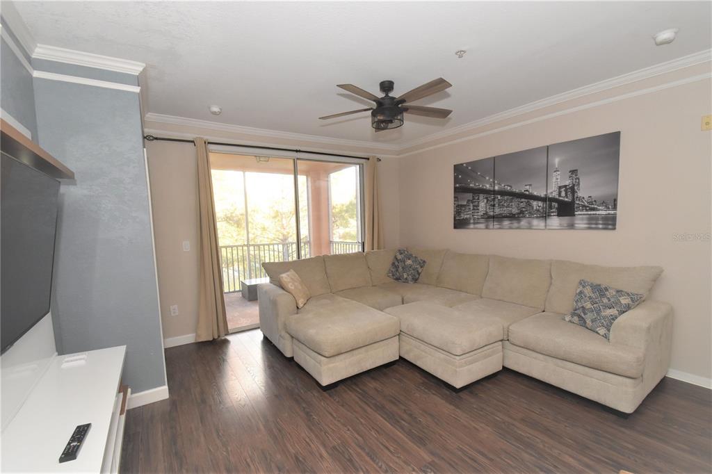 A living room features a beige sectional sofa, dark wood flooring, and a sliding glass door — 4178 CENTRAL SARASOTA PARKWAY UNIT 324, SARASOTA, FL