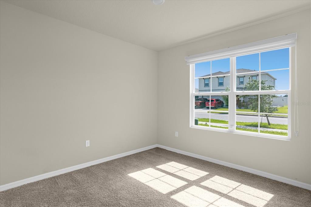 An empty bedroom with beige walls, gray carpet, and a window overlooking a suburban street — 285 SUMMERSHORE DRIVE, AUBURNDALE, FL