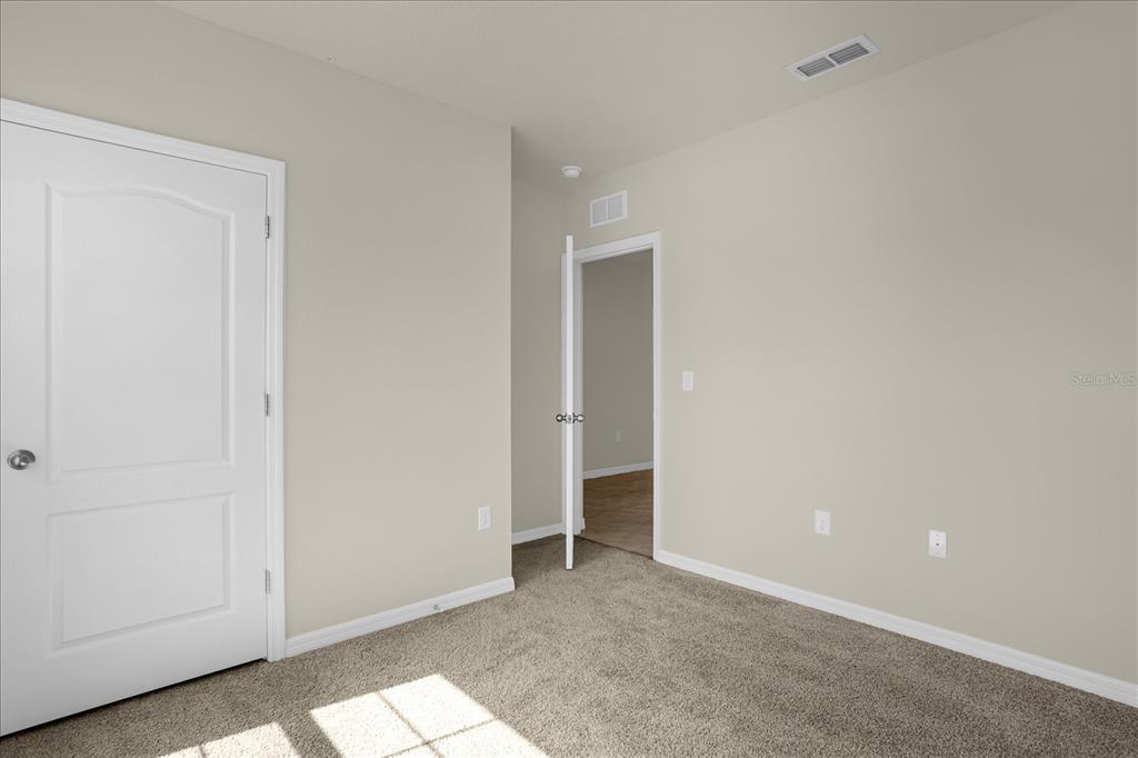 An empty bedroom features beige walls, tan carpeting, a white door, and an open doorway — 285 SUMMERSHORE DRIVE, AUBURNDALE, FL