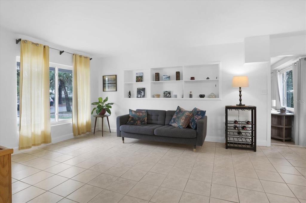 A living room with tile floors, a gray sofa, built-in shelving, and yellow curtains — 1032 NE 19TH PLACE, GAINESVILLE, FL