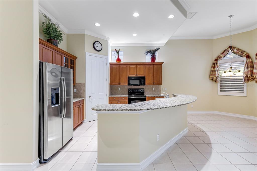 A kitchen features wood cabinets, granite countertops, stainless steel appliances, and a curved breakfast bar — 12584 GRANDEZZA CIRCLE, ESTERO, FL