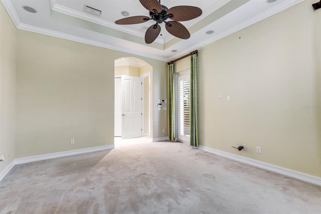 An empty room features beige walls, a tray ceiling with a fan, and carpeted flooring — 12584 GRANDEZZA CIRCLE, ESTERO, FL
