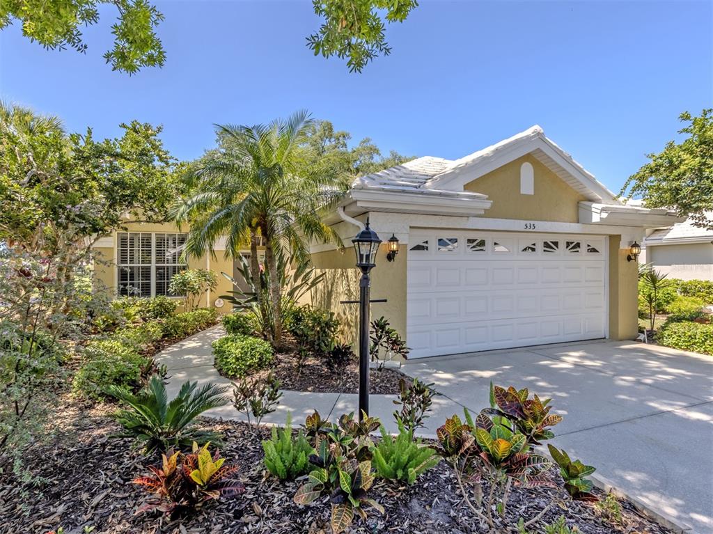 A single-story house with a white garage door, tan stucco exterior, and landscaped front yard — 535 FALLBROOK DRIVE, VENICE, FL