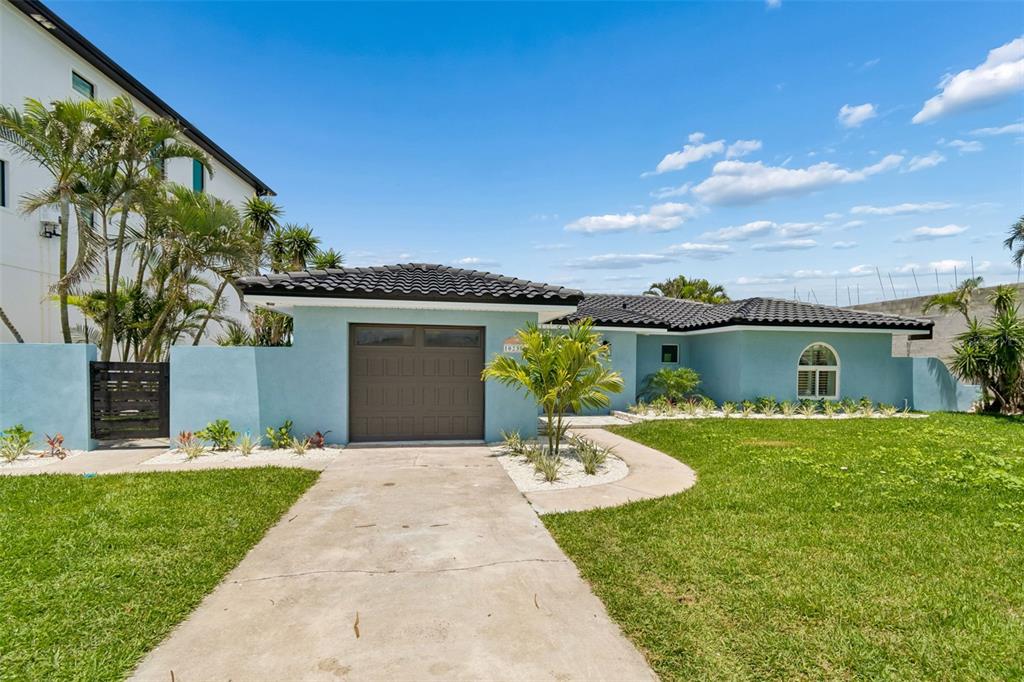 A light blue single-story house features a dark garage door and a curved concrete walkway — 10238 TARPON DRIVE, TREASURE ISLAND, FL