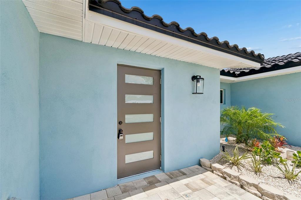 A light blue exterior wall features a brown front door with five horizontal glass panels — 10238 TARPON DRIVE, TREASURE ISLAND, FL