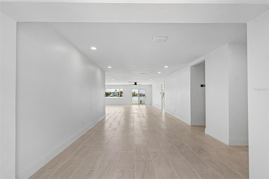 A long, open-concept room features white walls, recessed lighting, and light-colored wood-look tile flooring — 10238 TARPON DRIVE, TREASURE ISLAND, FL