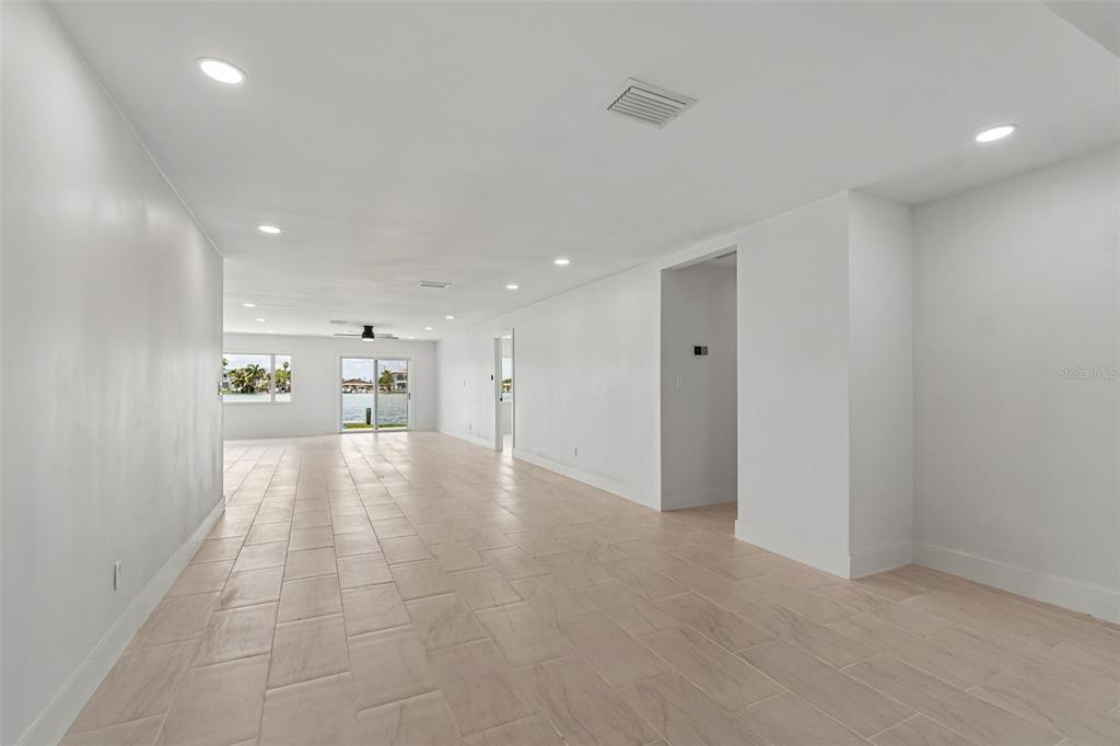 An empty, white-walled living area features light-colored tile flooring, recessed lighting, and water views — 10238 TARPON DRIVE, TREASURE ISLAND, FL
