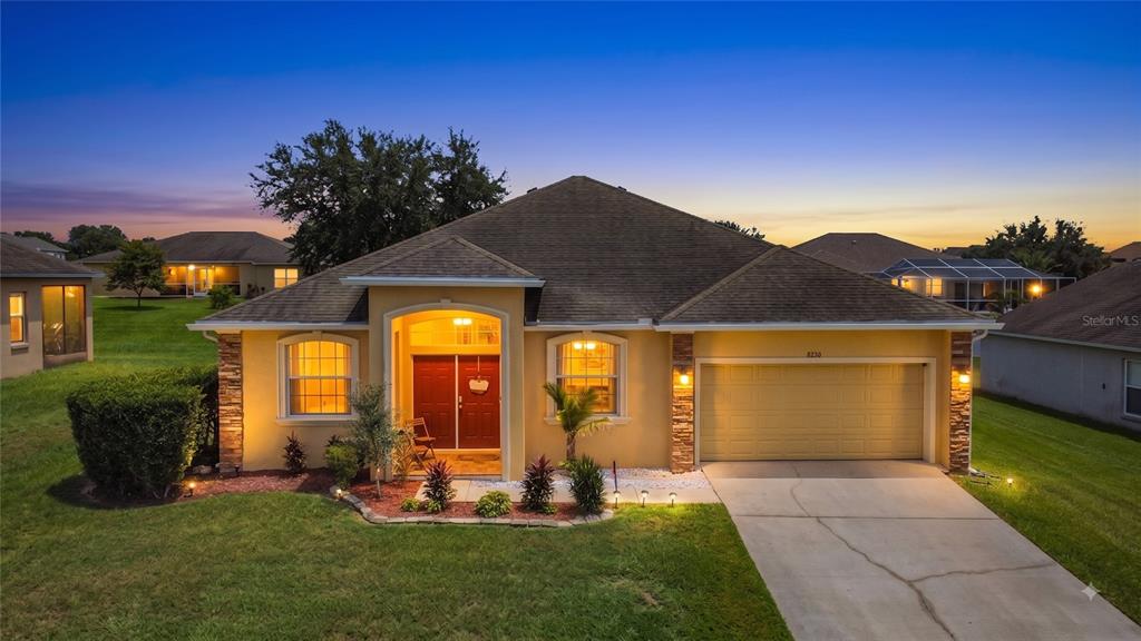 A single-story suburban house with a tan stucco exterior, a two-car garage, and a driveway — 8230 WOODVINE CIRCLE, LAKELAND, FL