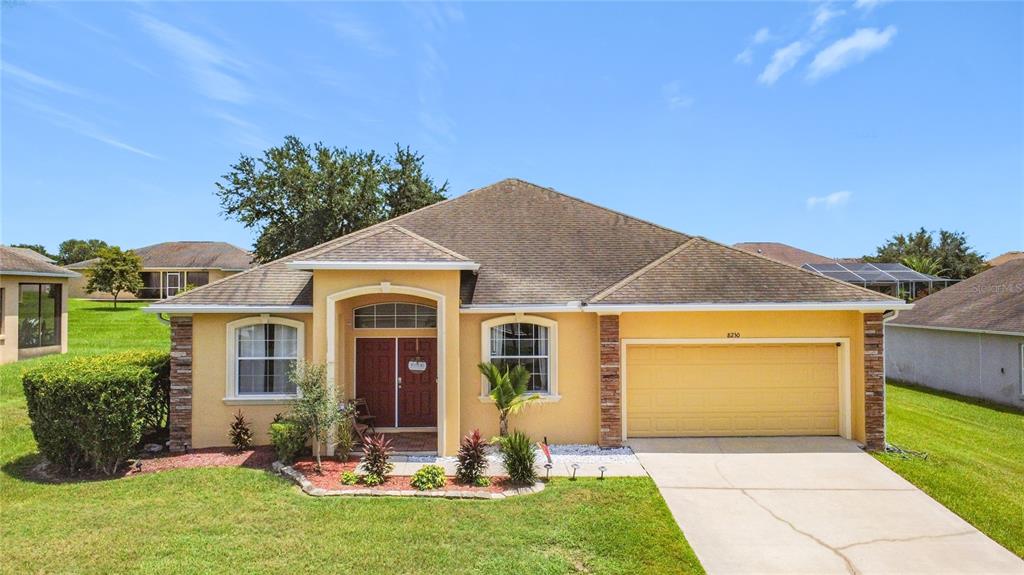 A single-story yellow stucco house with a two-car garage and a front entryway — 8230 WOODVINE CIRCLE, LAKELAND, FL