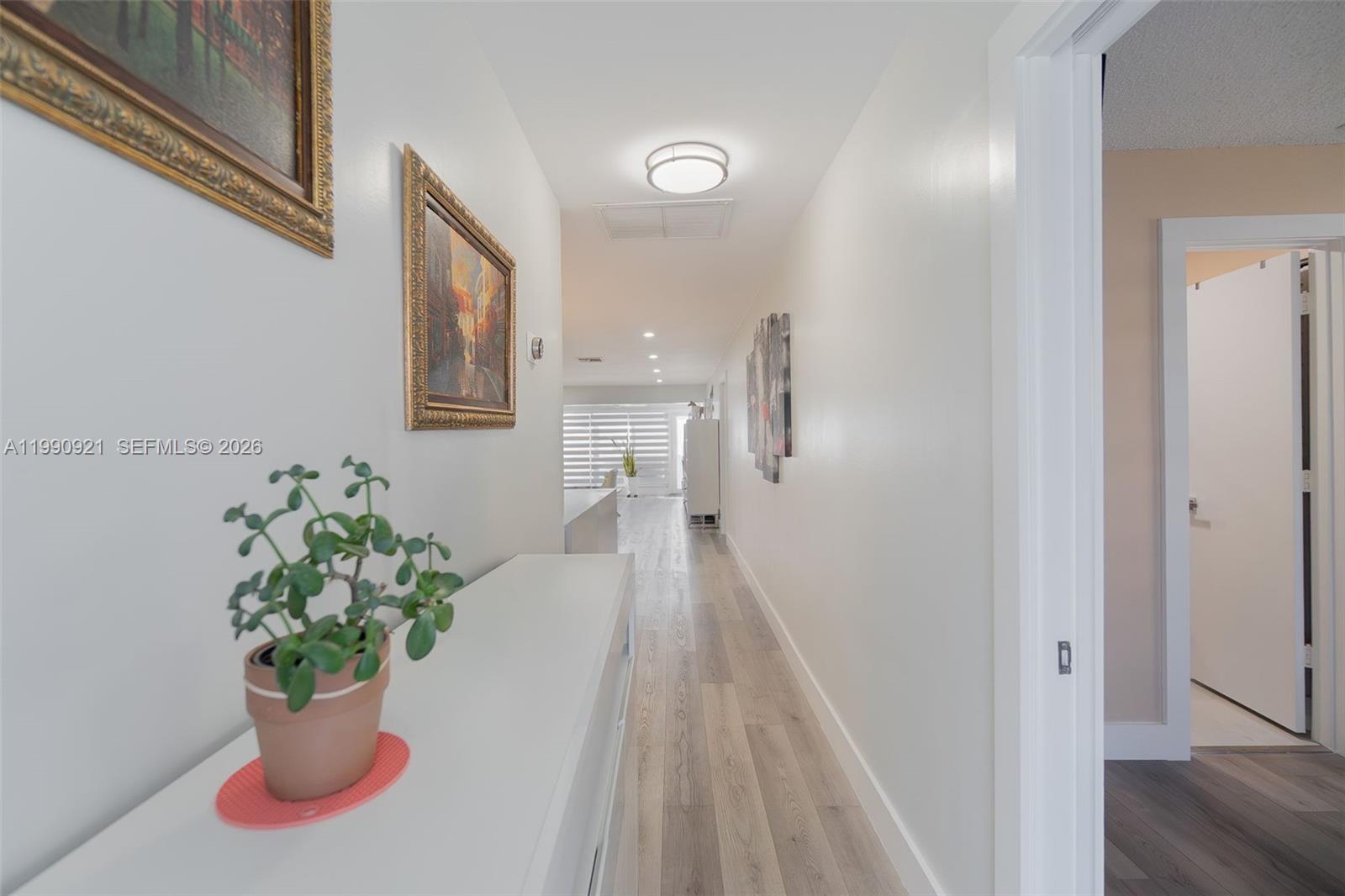 A hallway with light wood-look flooring leads toward a bright living area — 2400 Malayan Dr # D, Delray Beach FL 33445, DELRAY BEACH, FL