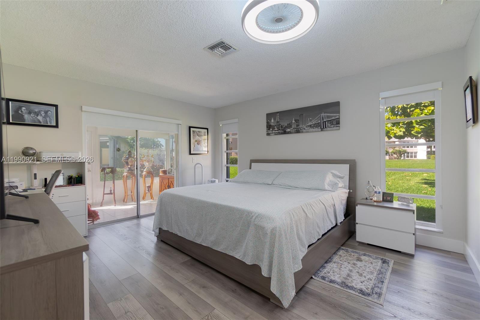 A bedroom features a platform bed, light wood-look flooring, and sliding glass doors to a patio — 2400 Malayan Dr # D, Delray Beach FL 33445, DELRAY BEACH, FL
