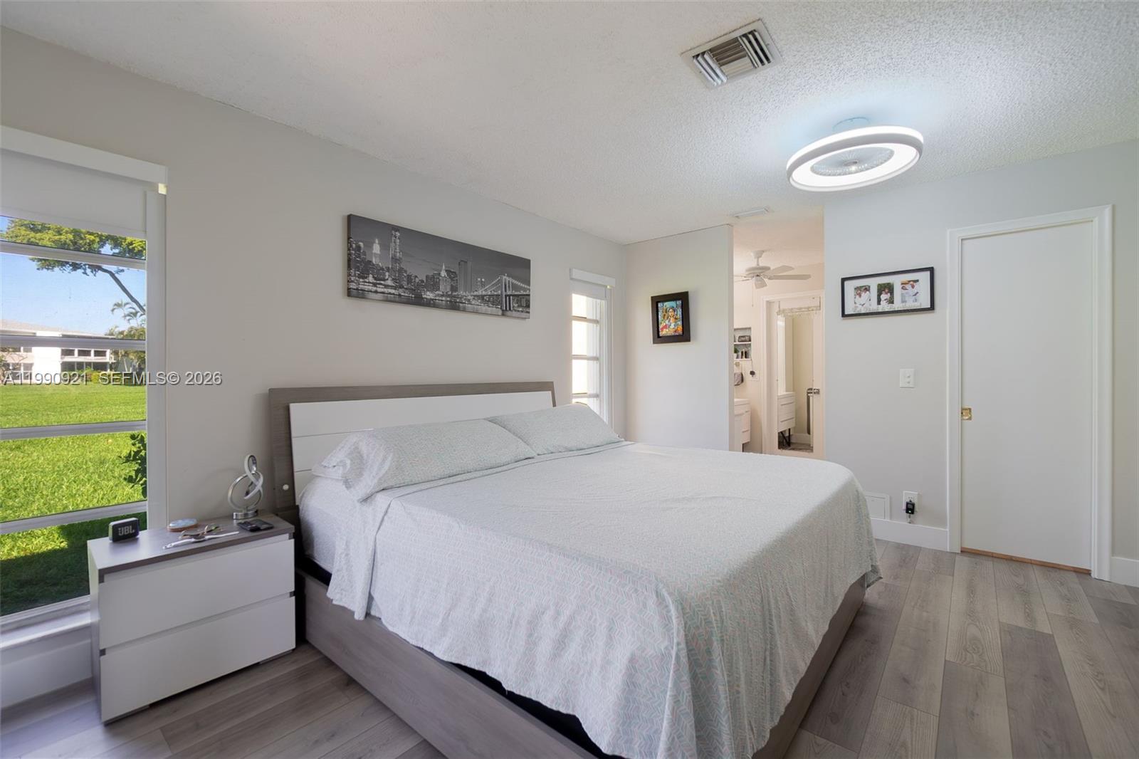 A bedroom features a bed, a nightstand, a window with a green view, and flooring — 2400 Malayan Dr # D, Delray Beach FL 33445, DELRAY BEACH, FL