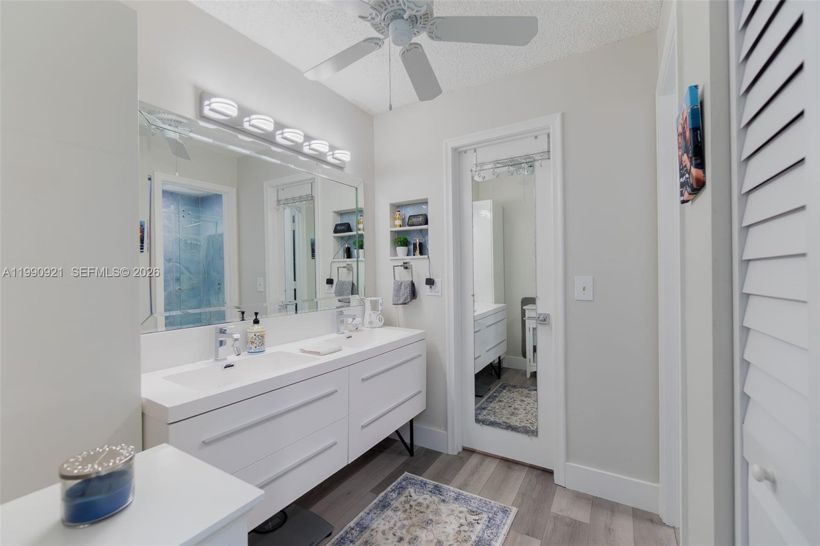 A modern bathroom features a double vanity, a large mirror, and a ceiling fan — 2400 Malayan Dr # D, Delray Beach FL 33445, DELRAY BEACH, FL