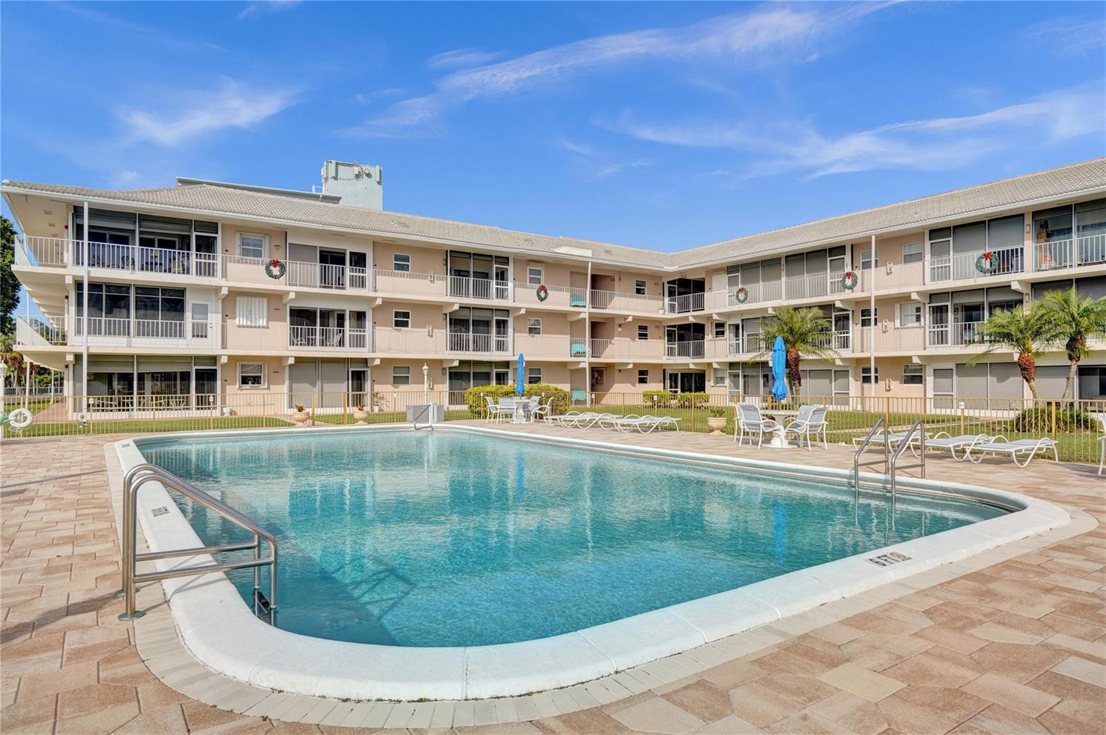 A swimming pool with a paved deck overlooks a canal lined with palm trees — 745 SE 19th Avenue # 134, Deerfield Beach FL 33441, DEERFIELD BEACH, FL