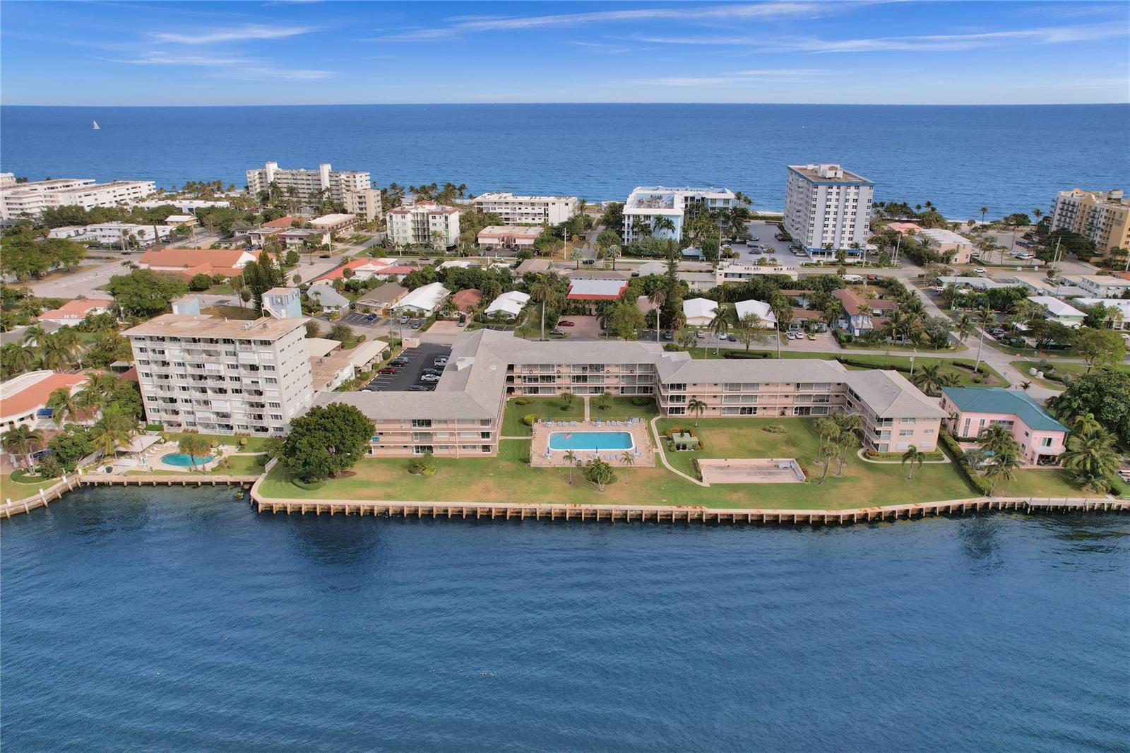 An aerial view shows a canal flowing between residential properties and apartment buildings toward the ocean — 745 SE 19th Avenue # 134, Deerfield Beach FL 33441, DEERFIELD BEACH, FL