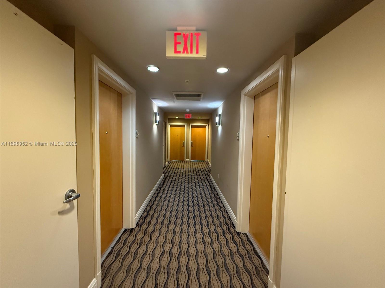 A narrow indoor hallway features patterned carpeting, beige walls, and several wooden doors — 244 Biscayne Blvd # 3708, Miami FL 33132, MIAMI, FL