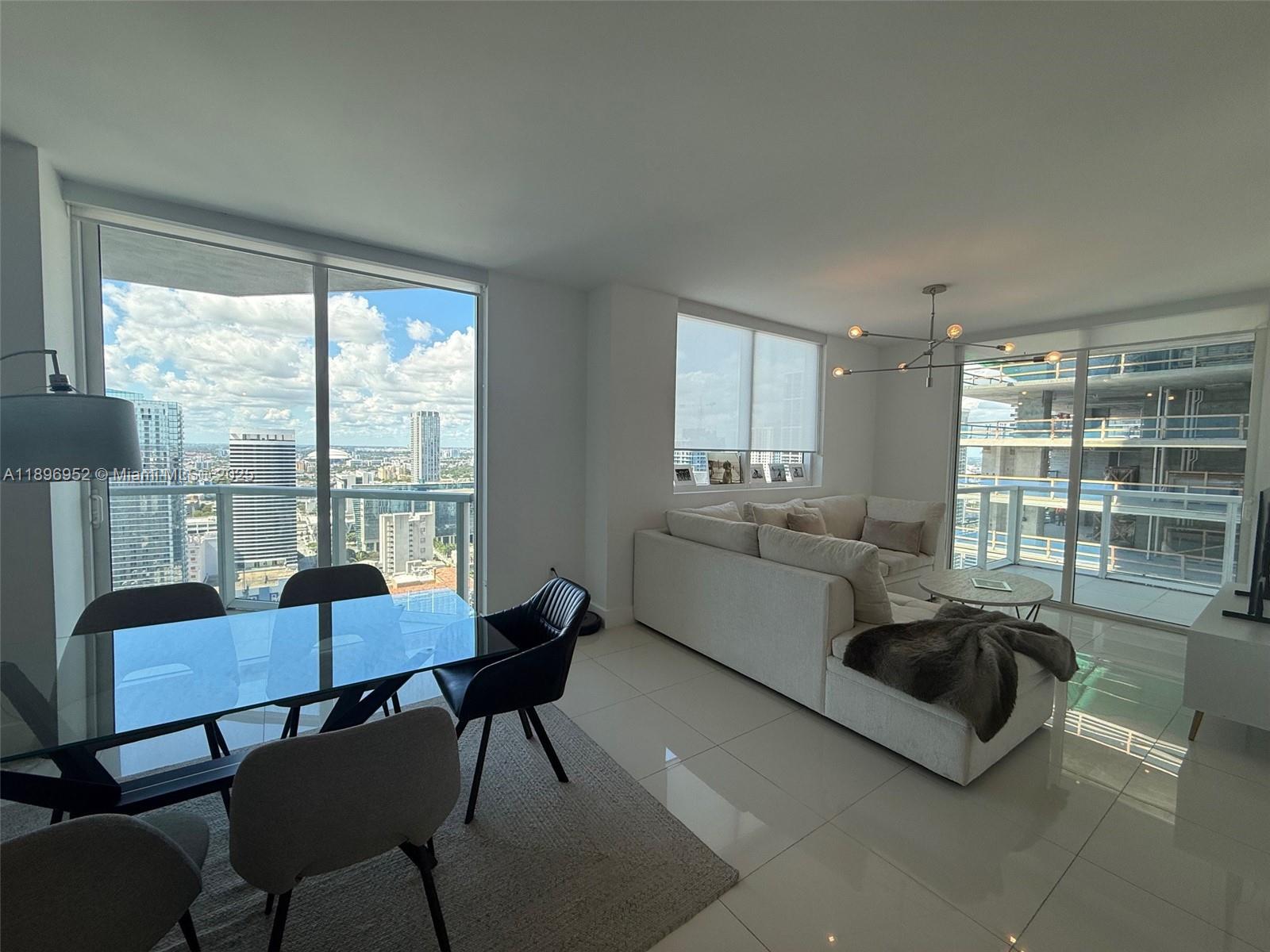 A modern living and dining area with floor-to-ceiling windows overlooking a city skyline — 244 Biscayne Blvd # 3708, Miami FL 33132, MIAMI, FL