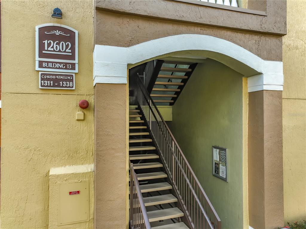 An exterior view of a condominium building entrance featuring a staircase leading to upper levels — 12602 CREST SPRINGS LANE UNIT 1333, ORLANDO, FL
