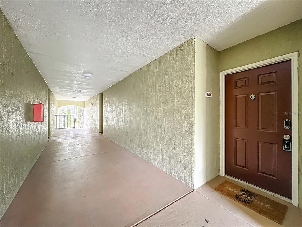 A covered exterior walkway leads to a brown front door with a welcome mat — 12602 CREST SPRINGS LANE UNIT 1333, ORLANDO, FL
