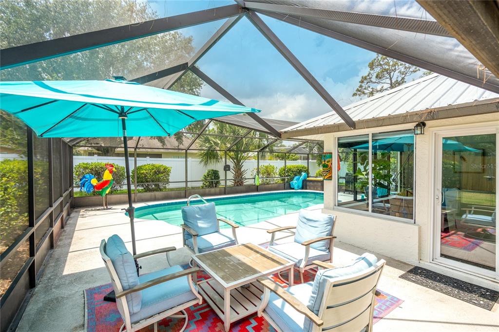 A screened-in patio features a swimming pool, outdoor furniture, and a bright blue umbrella — 54 FORDHAM LANE, PALM COAST, FL