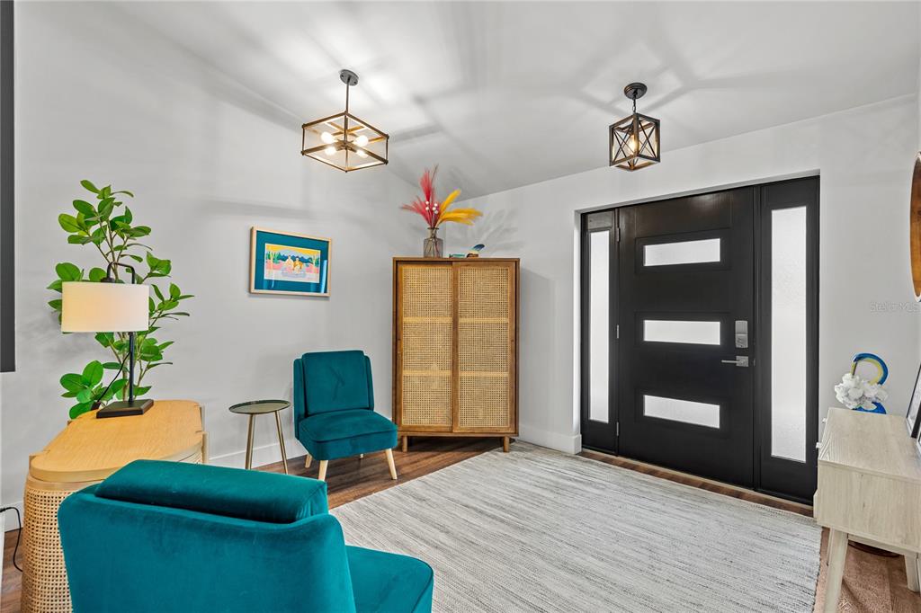A modern entryway features two teal velvet chairs, a rattan cabinet, and a black front door — 54 FORDHAM LANE, PALM COAST, FL