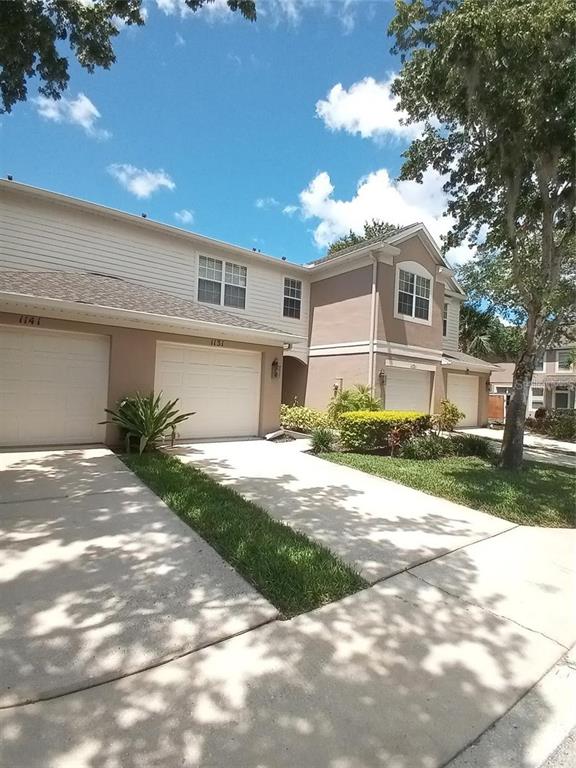 A two-story townhouse exterior with beige siding, stucco walls, and two attached garages — 1121 SETON HALL COURT, SANFORD, FL