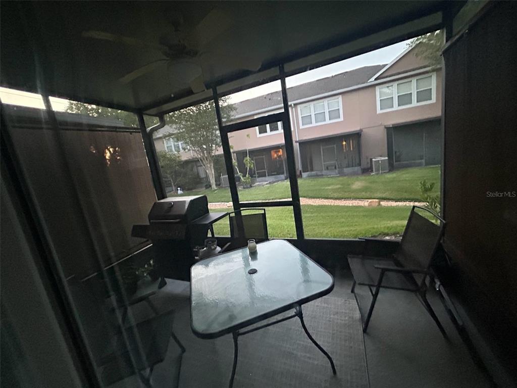 A screened-in patio features a glass-top table, chairs, and a grill overlooking a grassy lawn — 1121 SETON HALL COURT, SANFORD, FL