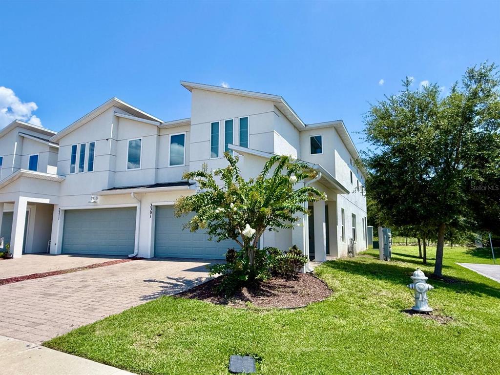 A two-story townhouse with a light-colored exterior, two garage doors, and a front yard — 3301 BEAU ROAD, KISSIMMEE, FL