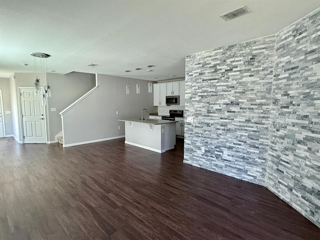 An open-concept kitchen and living area features dark wood flooring and a gray stone accent wall — 3301 BEAU ROAD, KISSIMMEE, FL