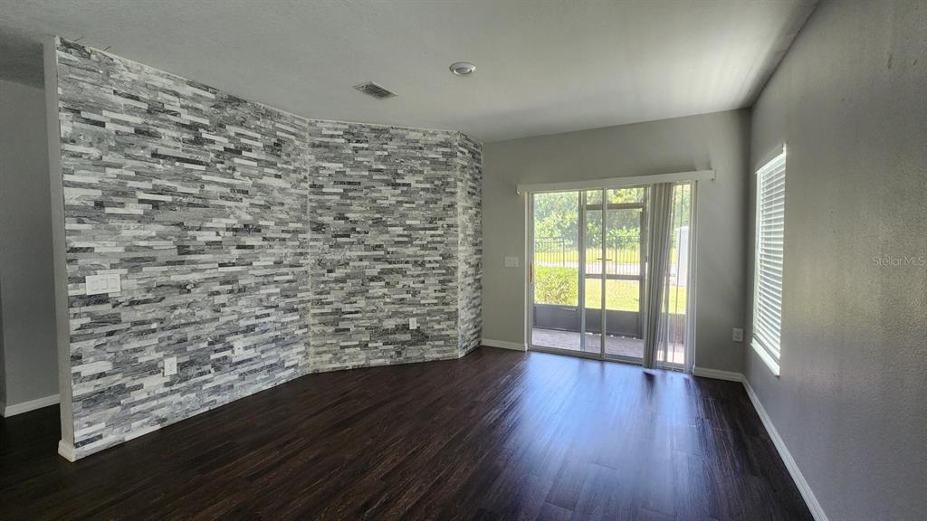 A room with dark wood flooring, a gray stone accent wall, and sliding glass doors — 3301 BEAU ROAD, KISSIMMEE, FL