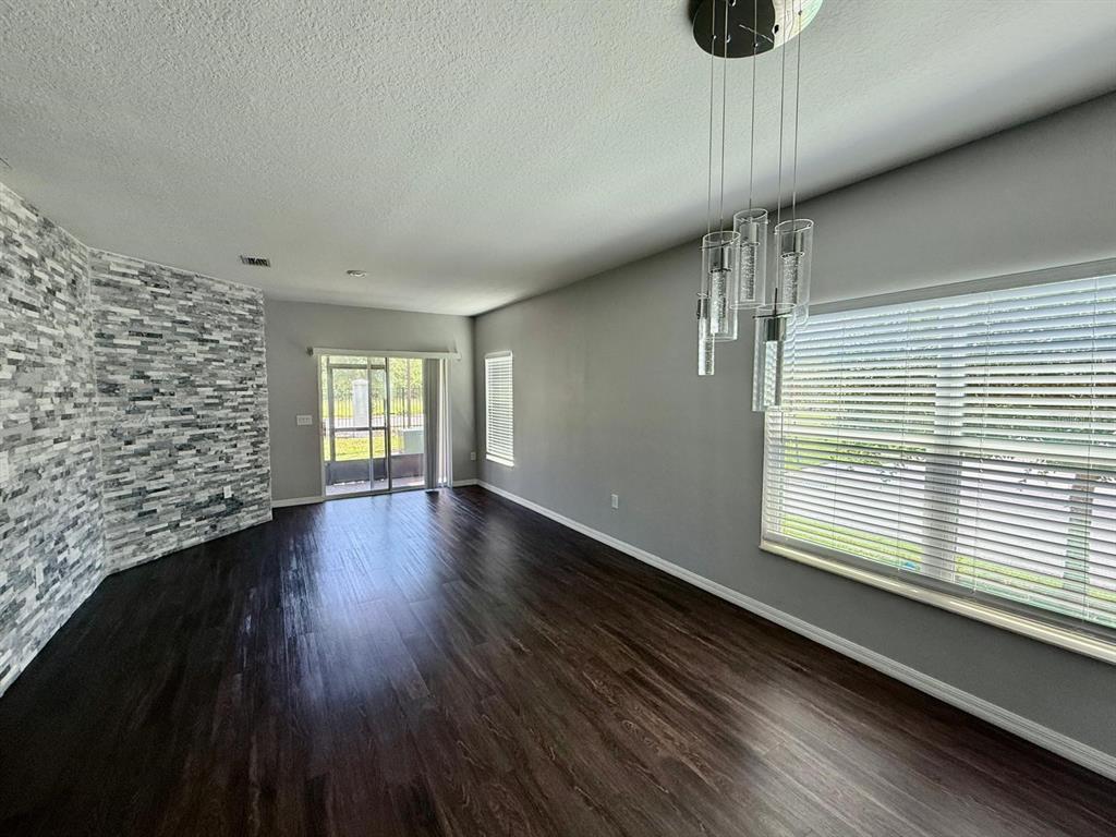 A dining area with dark wood floors, a stone accent wall, and a modern pendant light — 3301 BEAU ROAD, KISSIMMEE, FL