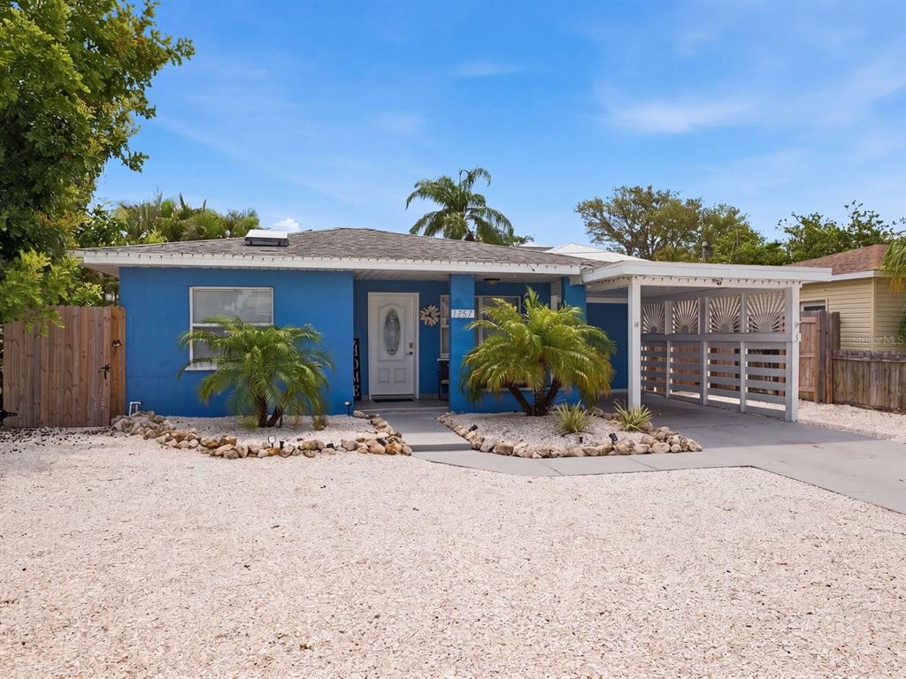A blue single-story house features a white front door, a carport, and a gravel yard — 1207 1ST STREET, INDIAN ROCKS BEACH, FL