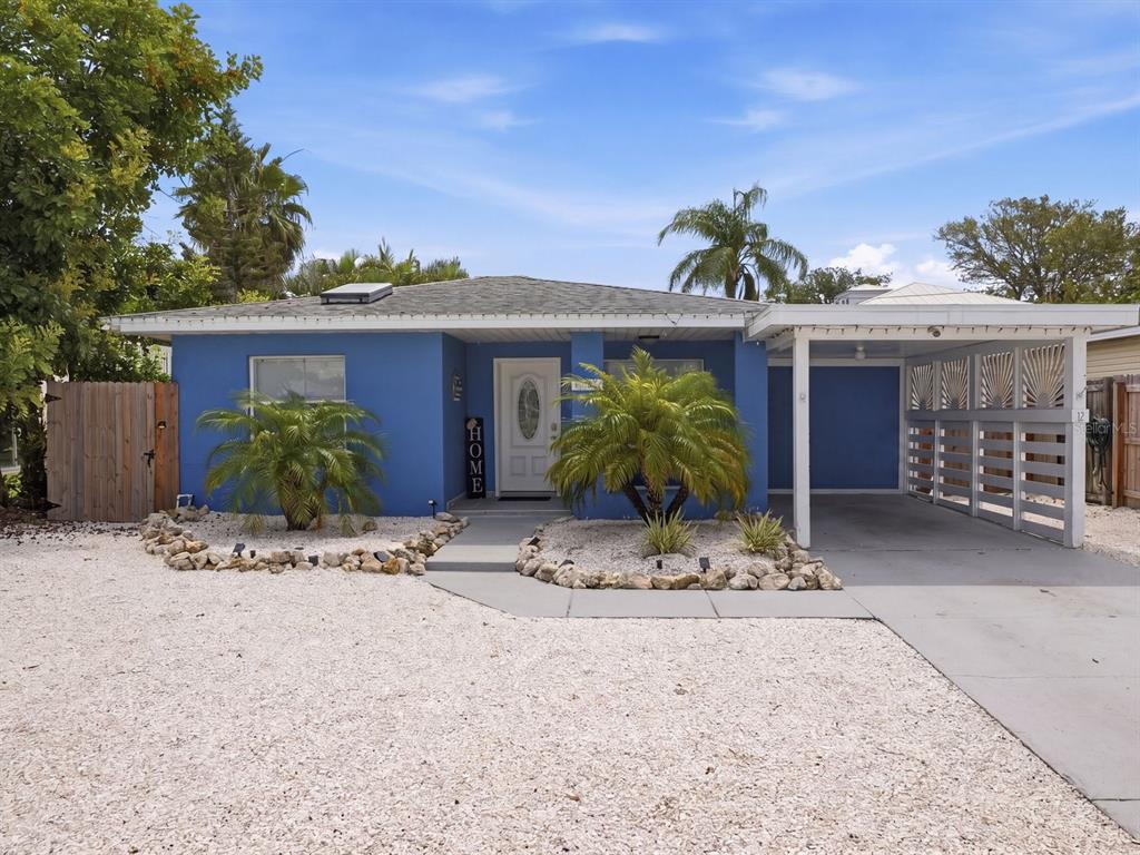 A blue single-story house features a gravel front yard, palm trees, and a white carport — 1207 1ST STREET, INDIAN ROCKS BEACH, FL