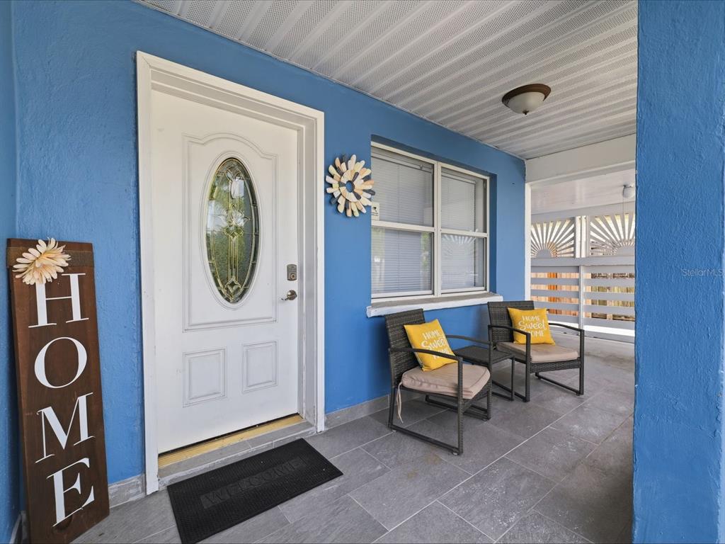 A blue-painted front porch features a white door, two chairs, and gray tiled flooring — 1207 1ST STREET, INDIAN ROCKS BEACH, FL