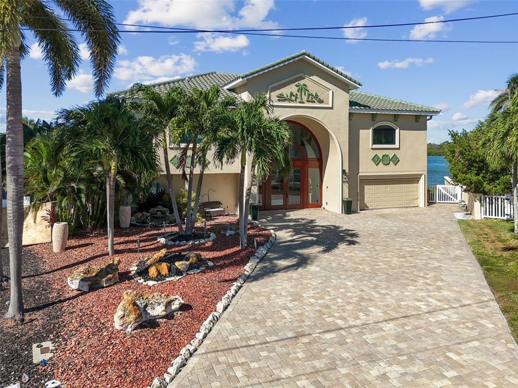A two-story house with a paved driveway, palm trees, and a red rock landscape — 582 JOHNS PASS AVENUE, MADEIRA BEACH, FL