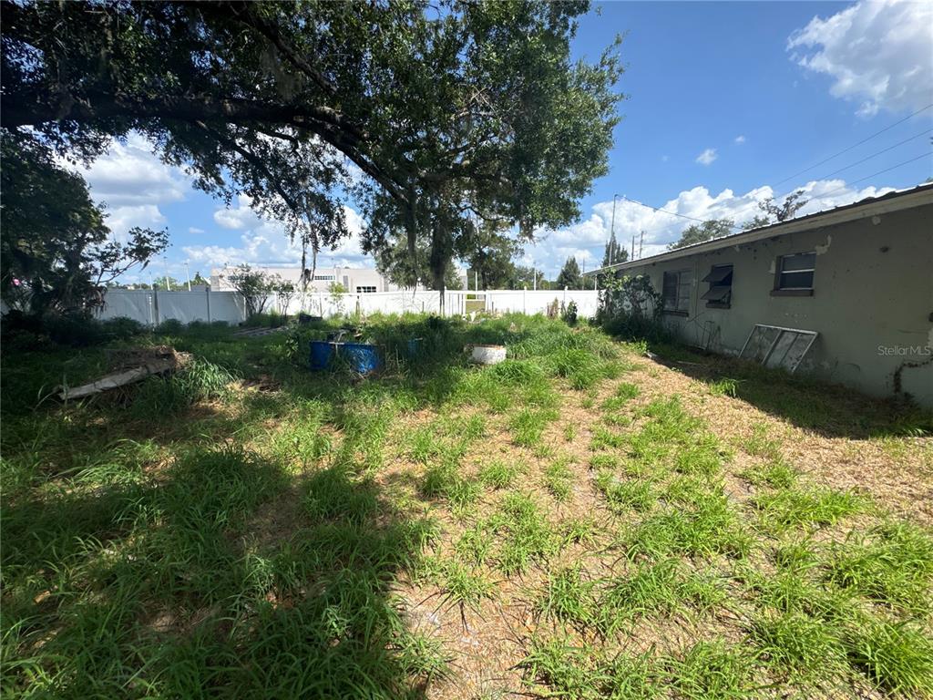 An overgrown backyard features a large tree, a white vinyl fence, and a house exterior — 2152 SE CARLSTROM FIELD ROAD, ARCADIA, FL