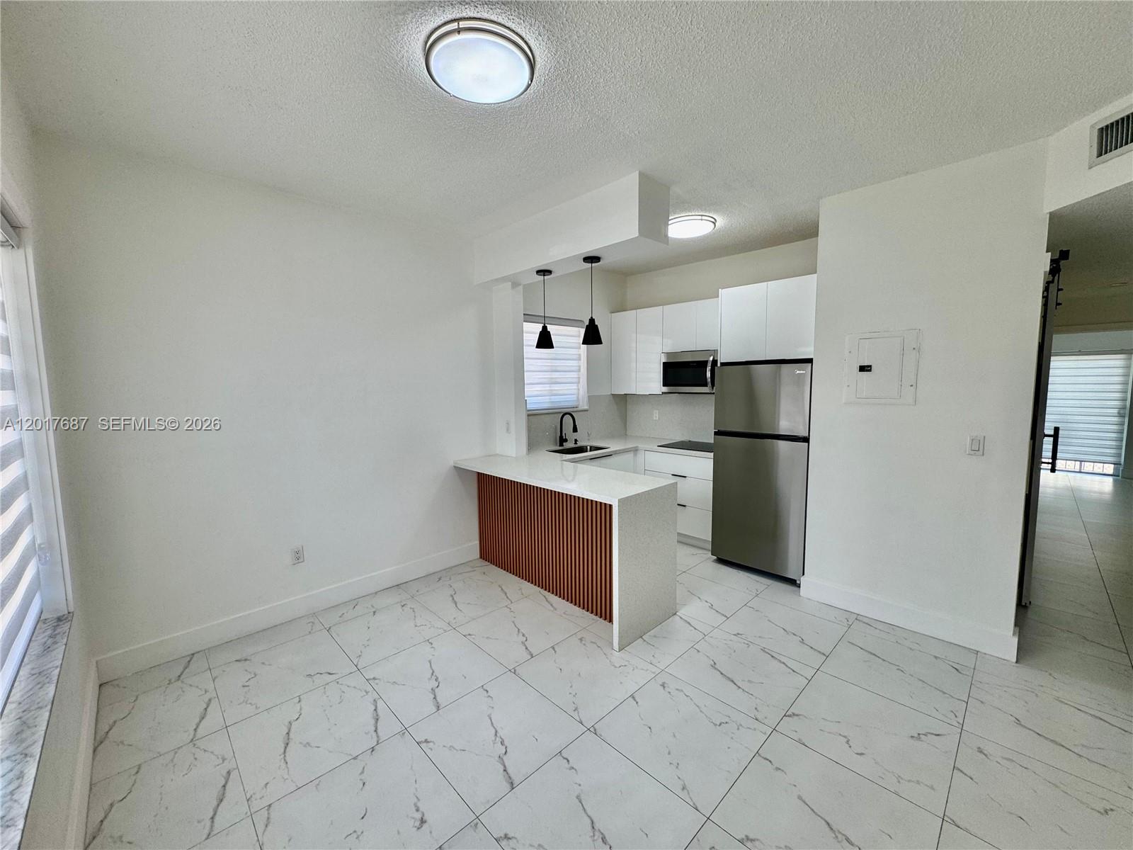 A kitchen features white cabinets, stainless steel appliances, a wood-slatted peninsula, and marble-patterned tile floors — 421 NW 13th Ave # A, Miami FL 33125, MIAMI, FL