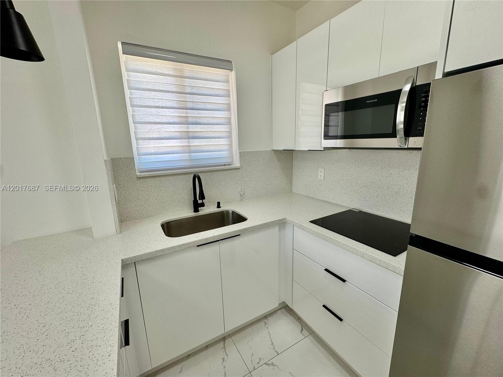 A modern kitchen features white cabinets, speckled countertops, stainless steel appliances, and a black faucet — 421 NW 13th Ave # A, Miami FL 33125, MIAMI, FL