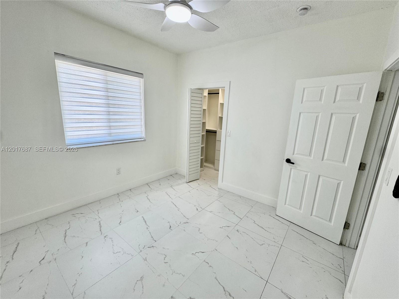 A bedroom features white walls, marble-patterned tile flooring, a ceiling fan, and a walk-in closet — 421 NW 13th Ave # A, Miami FL 33125, MIAMI, FL