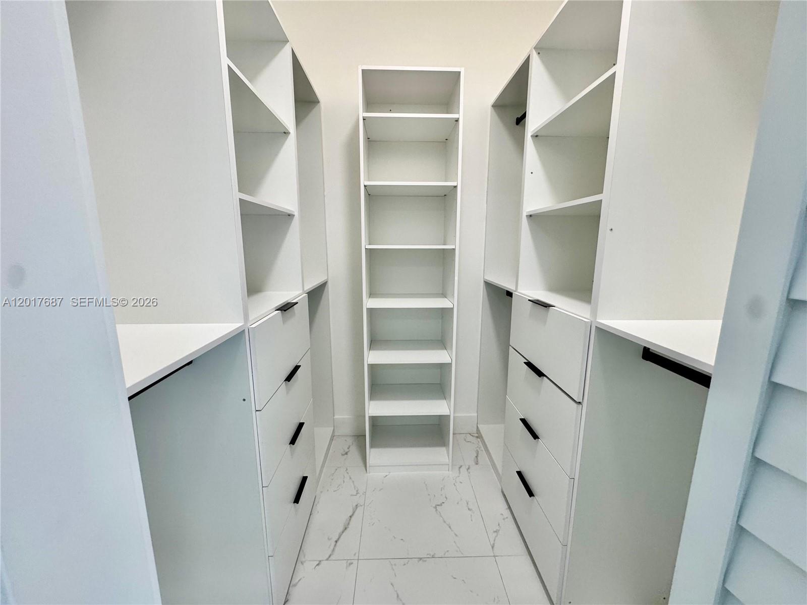 A walk-in closet features white shelving, built-in drawers with black hardware, and marble-look tile flooring — 421 NW 13th Ave # A, Miami FL 33125, MIAMI, FL