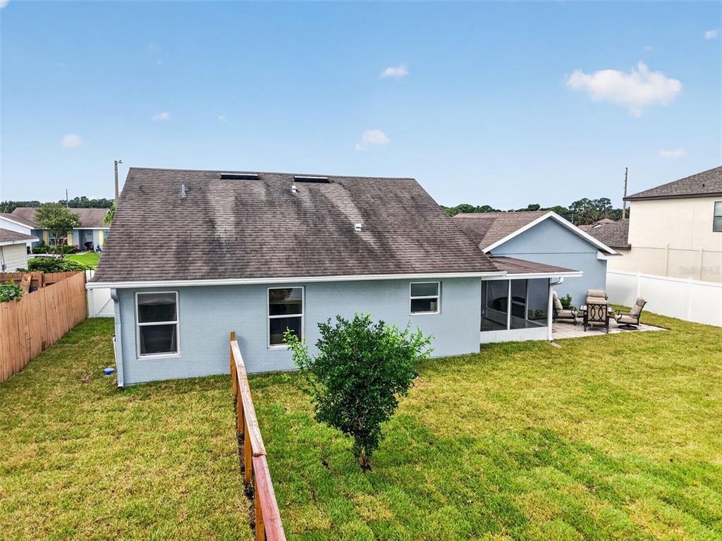 The rear exterior of a light blue house features a shingled roof and fenced yard — 544 TORTOLA AVENUE, TAVARES, FL