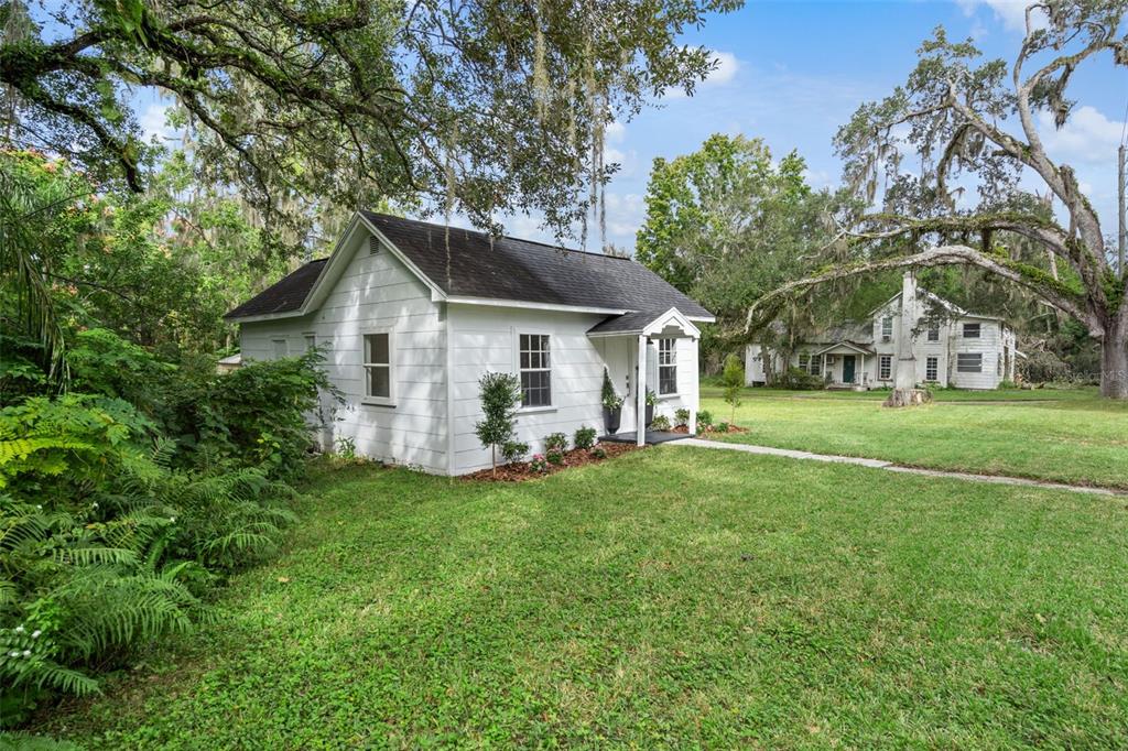 A white cottage with a dark roof sits on a grassy lawn near another house — 515 STAFFORD AVENUE, BROOKSVILLE, FL