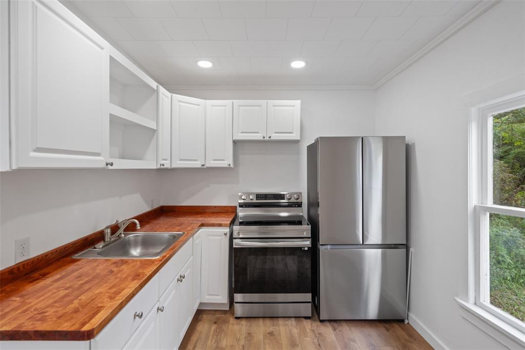 A kitchen features white cabinets, a wood countertop, stainless steel appliances, and wood-look flooring — 515 STAFFORD AVENUE, BROOKSVILLE, FL