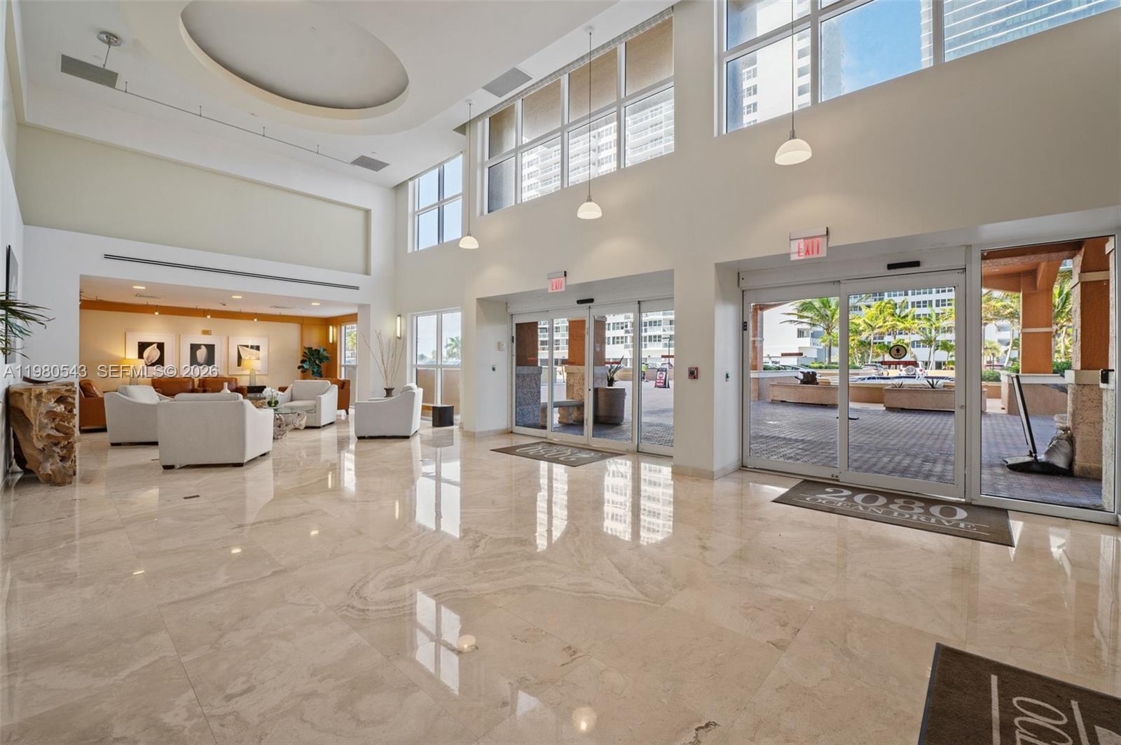 A spacious lobby features high ceilings, marble flooring, and glass doors leading to an outdoor area — 2080 S Ocean Dr # 1402, Hallandale Beach FL 33009, HALLANDALE BEACH, FL