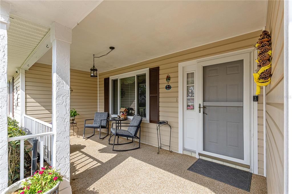 A covered front porch features tan siding, a screen door, and two rocking chairs — 8145 SW 108 STREET, OCALA, FL