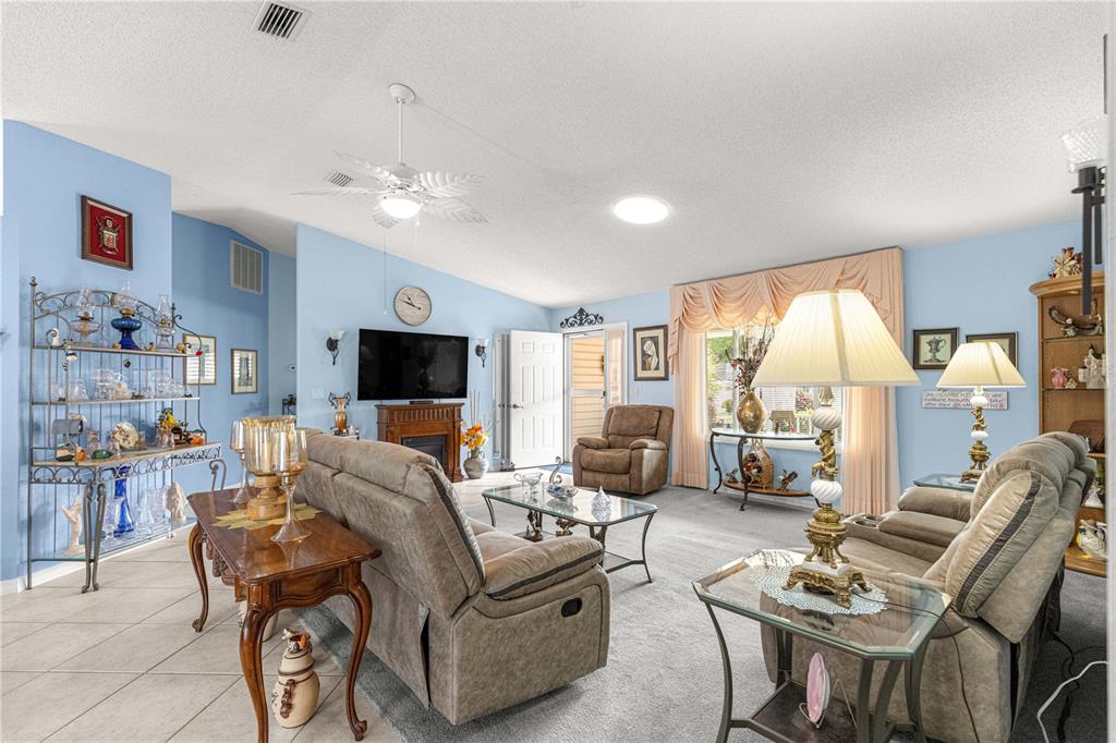 A living room with light blue walls, carpeted flooring, a ceiling fan, and traditional furniture — 8145 SW 108 STREET, OCALA, FL