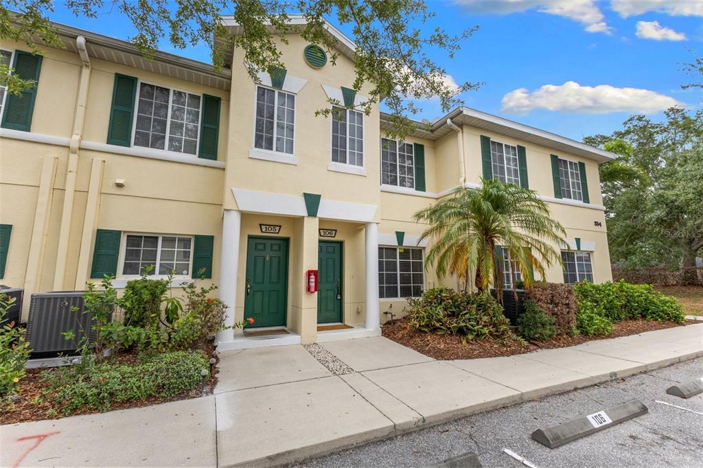 A two-story townhouse exterior features green doors, matching shutters, and a small palm tree — 354 CAPE HARBOUR LOOP UNIT 106, BRADENTON, FL