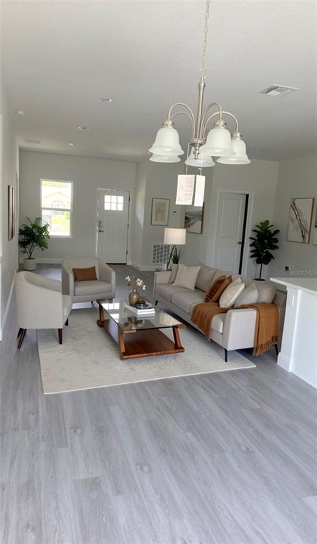 A living room features light wood-look flooring, a neutral sofa, an armchair, and a chandelier — 2500 SW 156TH LANE ROAD, OCALA, FL