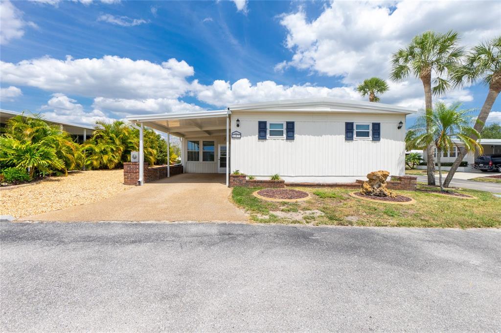 A single-story manufactured home features a carport, brick accents, and palm trees under a blue sky — 18 S DE LAS PALMAS STREET, ENGLEWOOD, FL