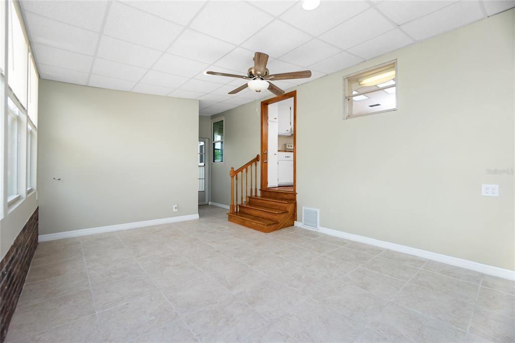 A room with light-colored tile flooring, a ceiling fan, and wooden stairs leading to a kitchen — 18 S DE LAS PALMAS STREET, ENGLEWOOD, FL
